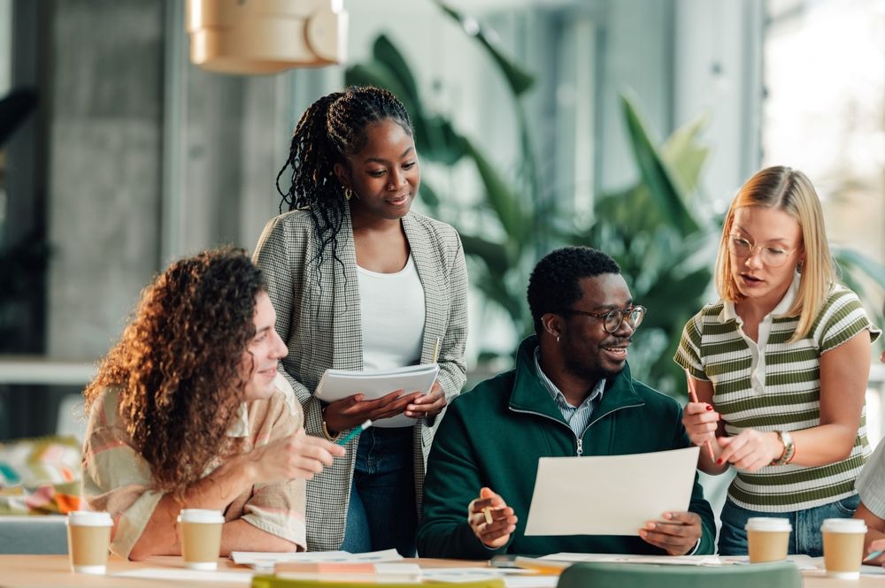 Des professionnels travaillent ensemble sur un projet, discutent d'idées et examinent des documents dans un bureau moderne.